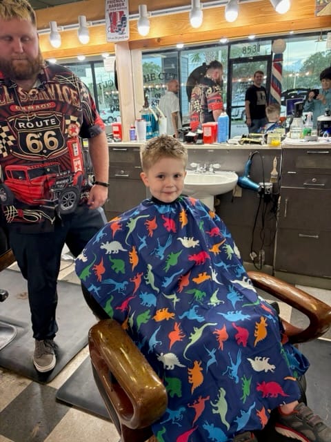 The boy smiling after his haircut, with Kyle beside him